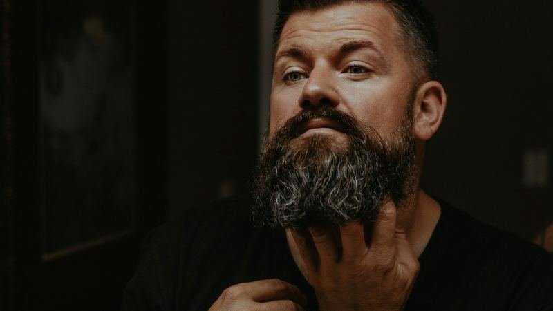 Мъж с гъста брада я разресва с пръсти у дома