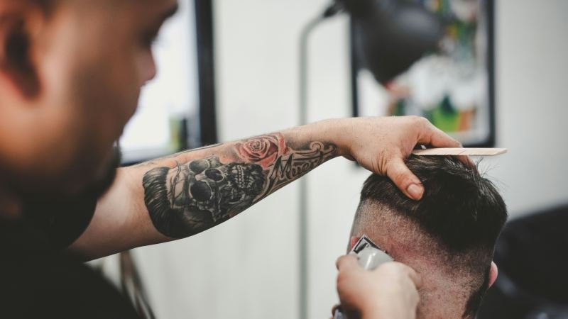 Бръснар оформя skin fade с машинка и гребен